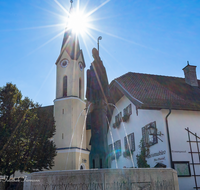 fileadmin/roha/images_galerie/orte_landschaft/Piding/PID-RUP-BR-0020-D-roha-Piding-Petersplatz-Rupertusbrunnen-Kirche-Sonne.png